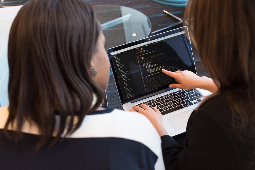Two women collaborating on coding using a web development platform on a laptop.