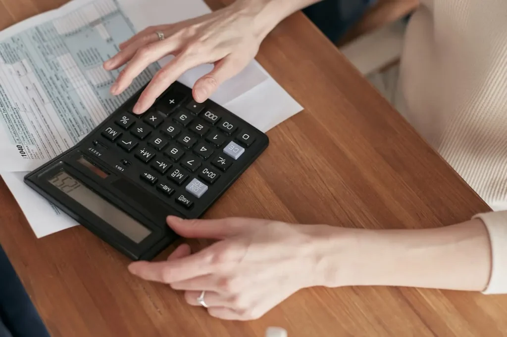 Close-up of hands using a calculator on top of financial documents during cost estimation.