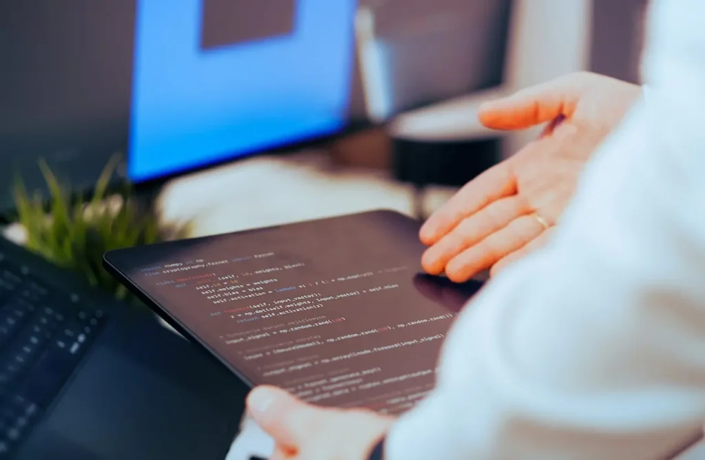 Developer reviewing code on tablet with laptop setup, representing modern app development and software engineering workflow.