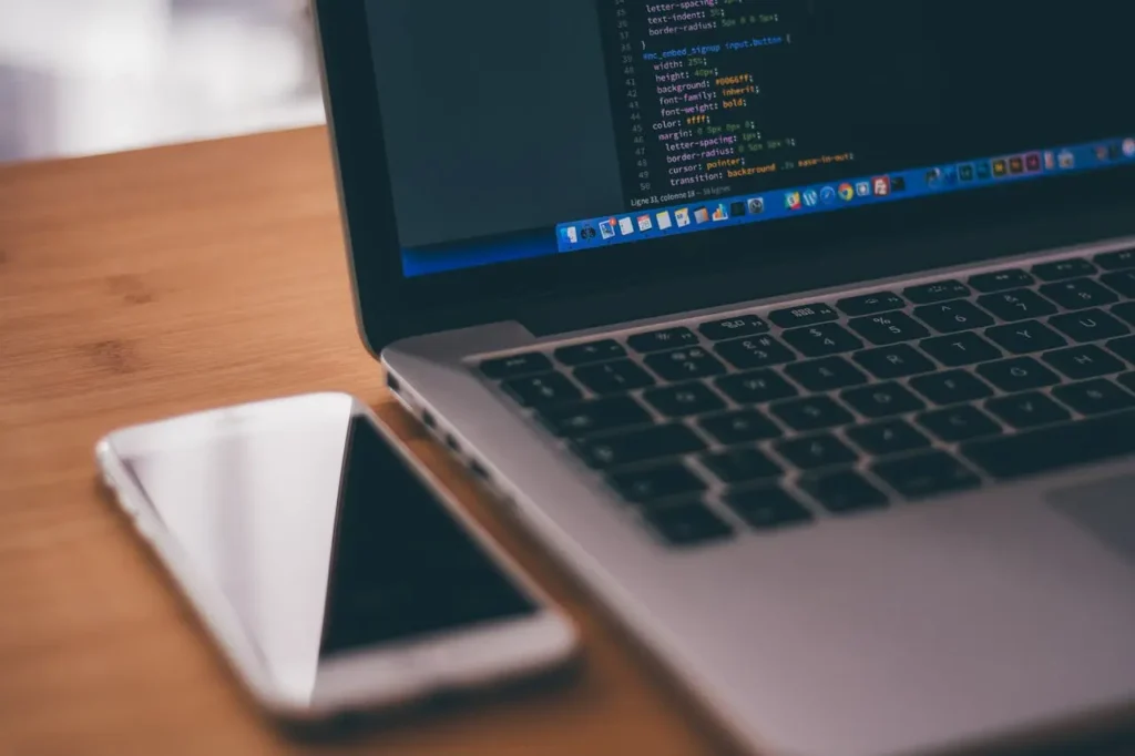 Laptop with code and mobile device, representing web application development and cross-device software solutions.