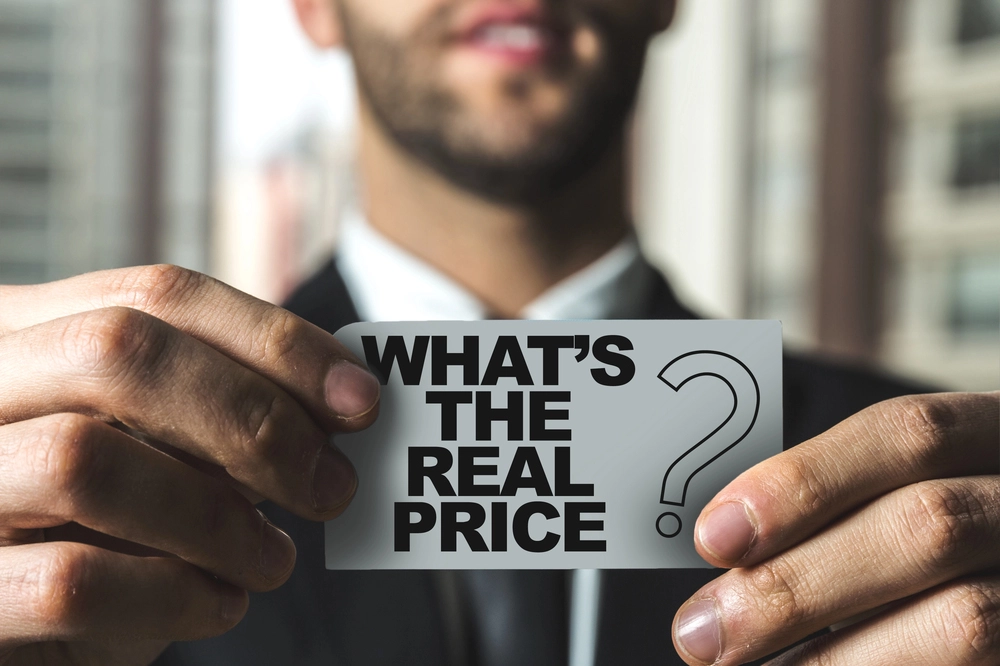 An image of a man holding a card that says "What's the price?", representing what is the actual price of creating an app.