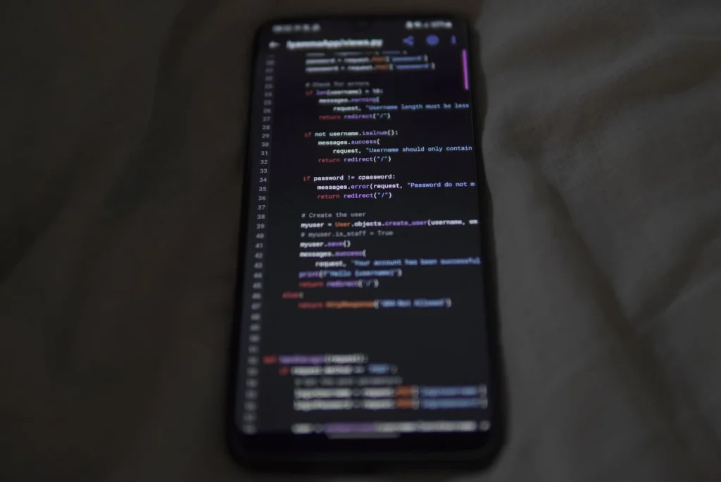 Smartphone displaying programming code on a dark screen, placed on grey fabric.